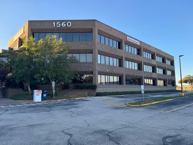 Exterior view of a brick office building labeled 1560 with large windows and a parking lot.