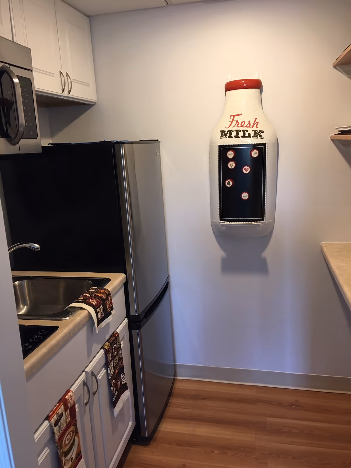 Small kitchen with fridge, stove, sink, and wall-mounted milk dispenser.