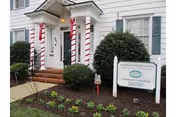 Front entrance of Norcroft Townhomes with striped columns, steps, greenery, and a sign.