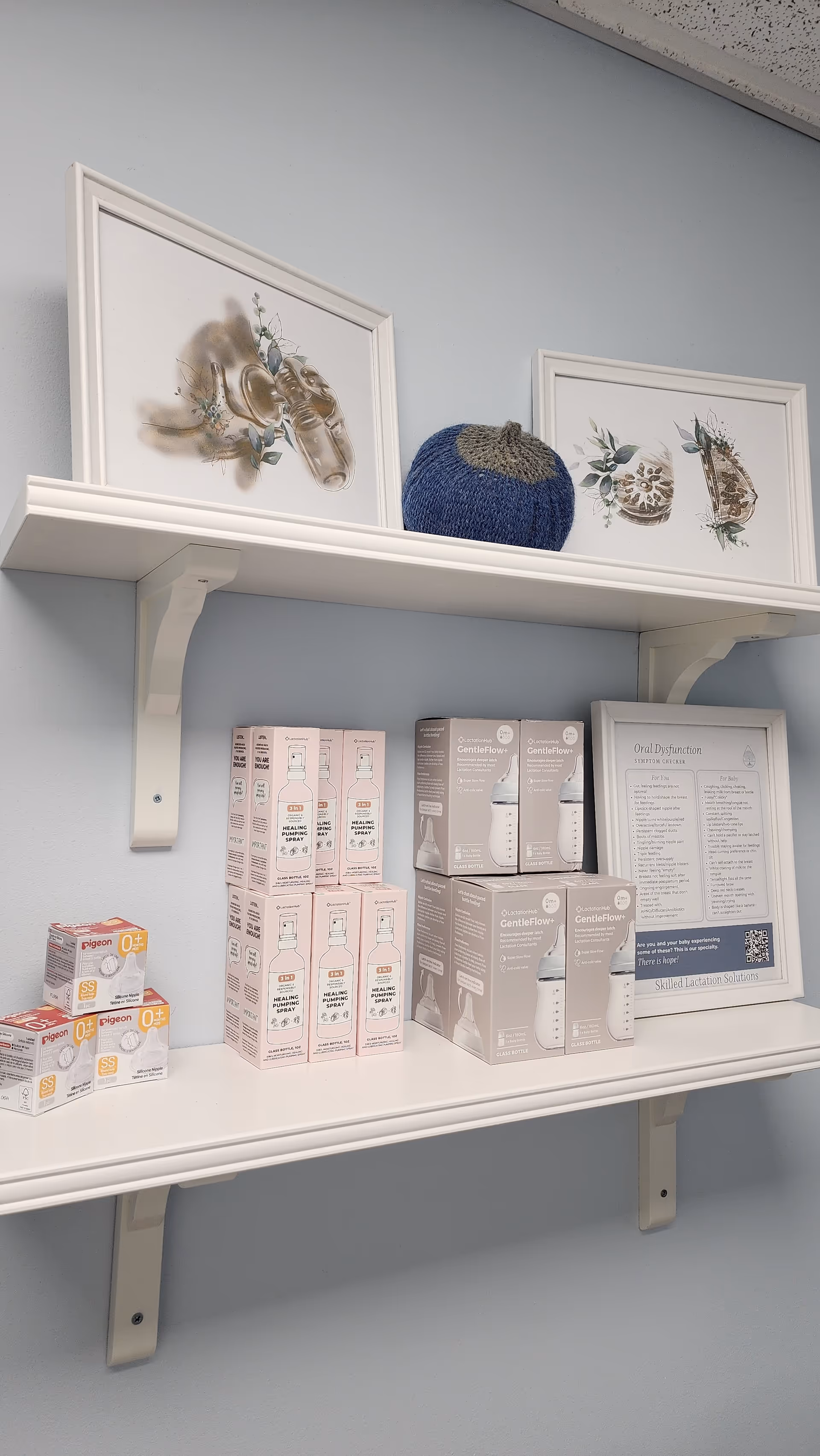 White shelf with framed art, a blue knitted cap, and assorted medical breast-pumping product boxes.
