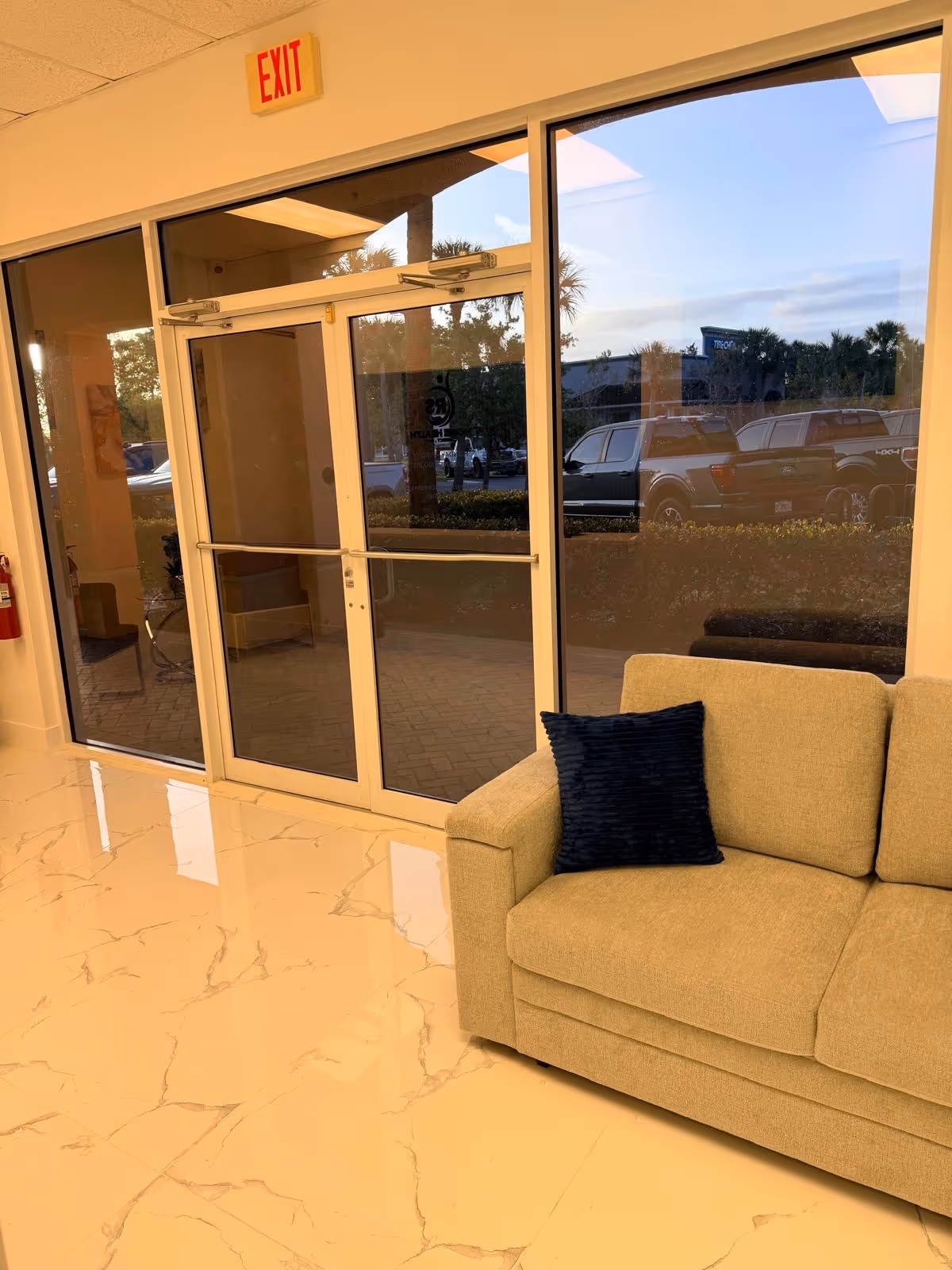 Lobby area with glass doors, exit sign, marble-like floors, and beige sofa.