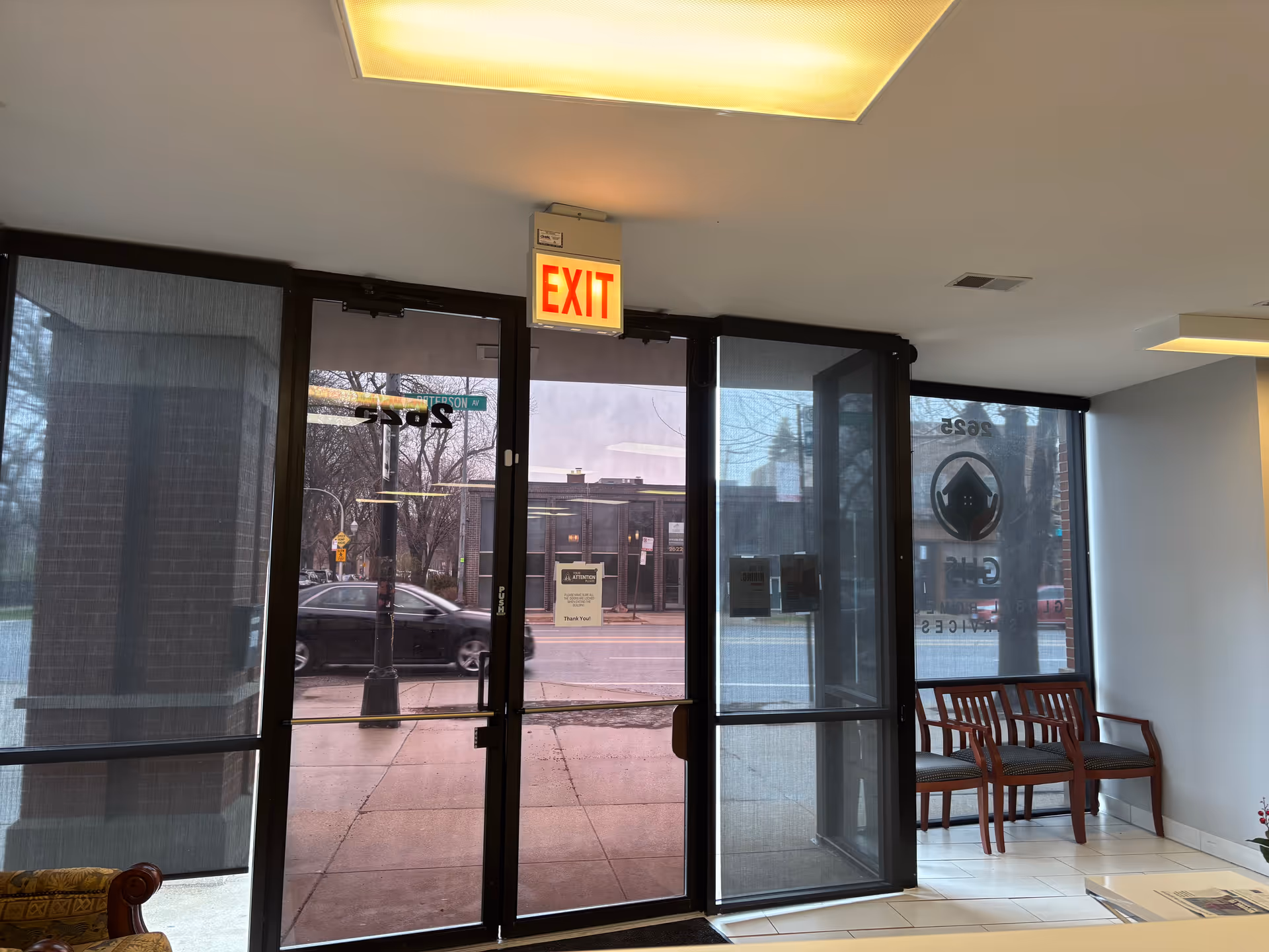 Lobby area with glass doors, an EXIT sign, and wooden chairs along the right.