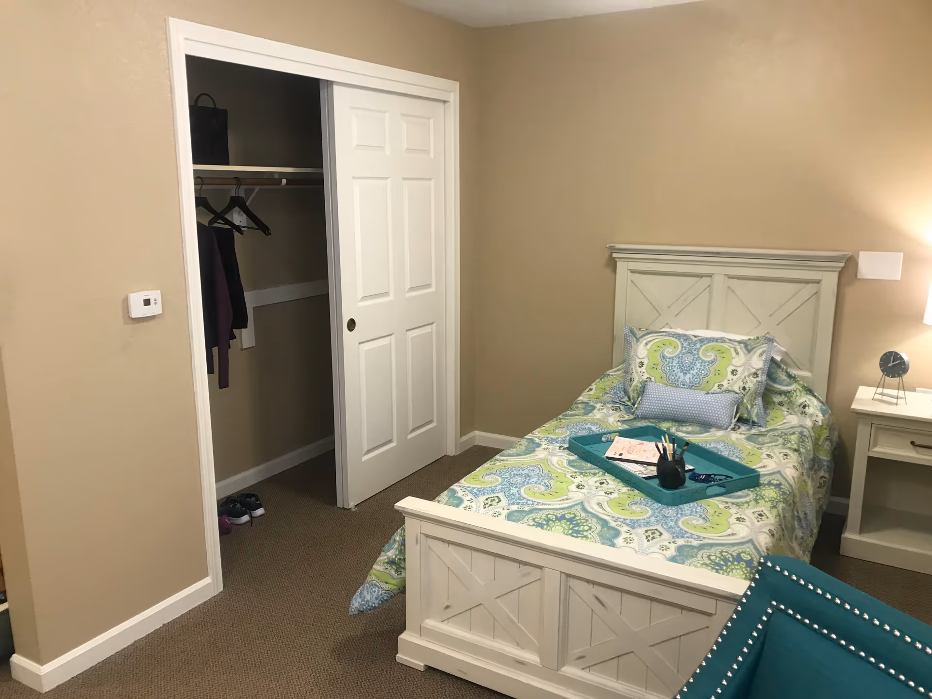 A clean bedroom in a senior living facility with a single bed and open closet.