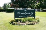 Exterior view of The Courtyards sign on a grassy lawn with trees