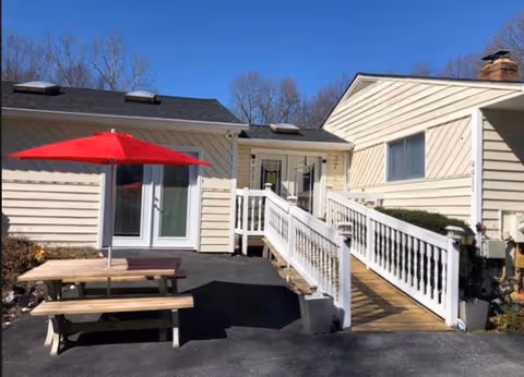 Exterior view of a senior living facility with ramp access and a red umbrella picnic table.