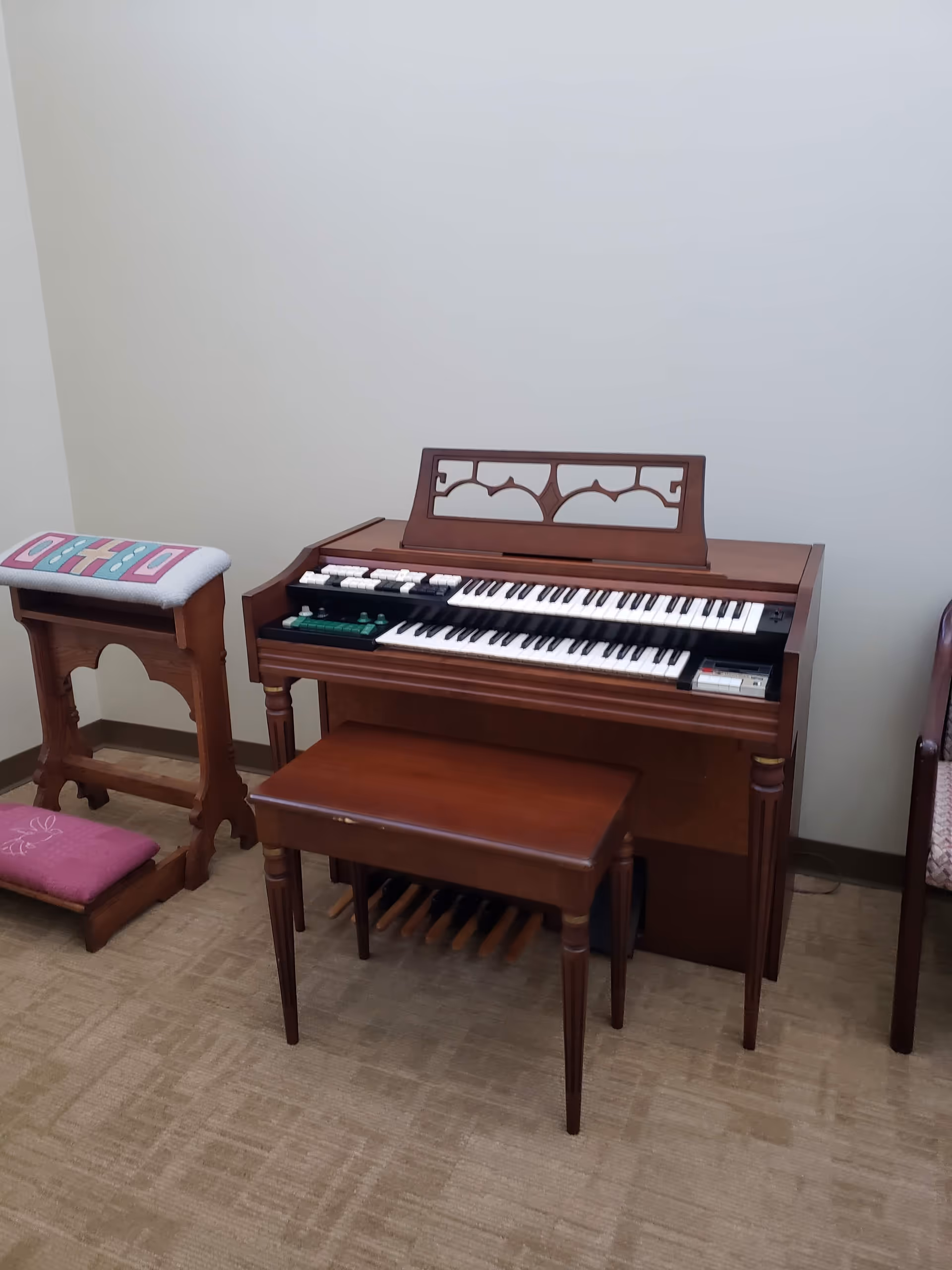 Wooden electronic organ with bench in a beige-carpeted room.