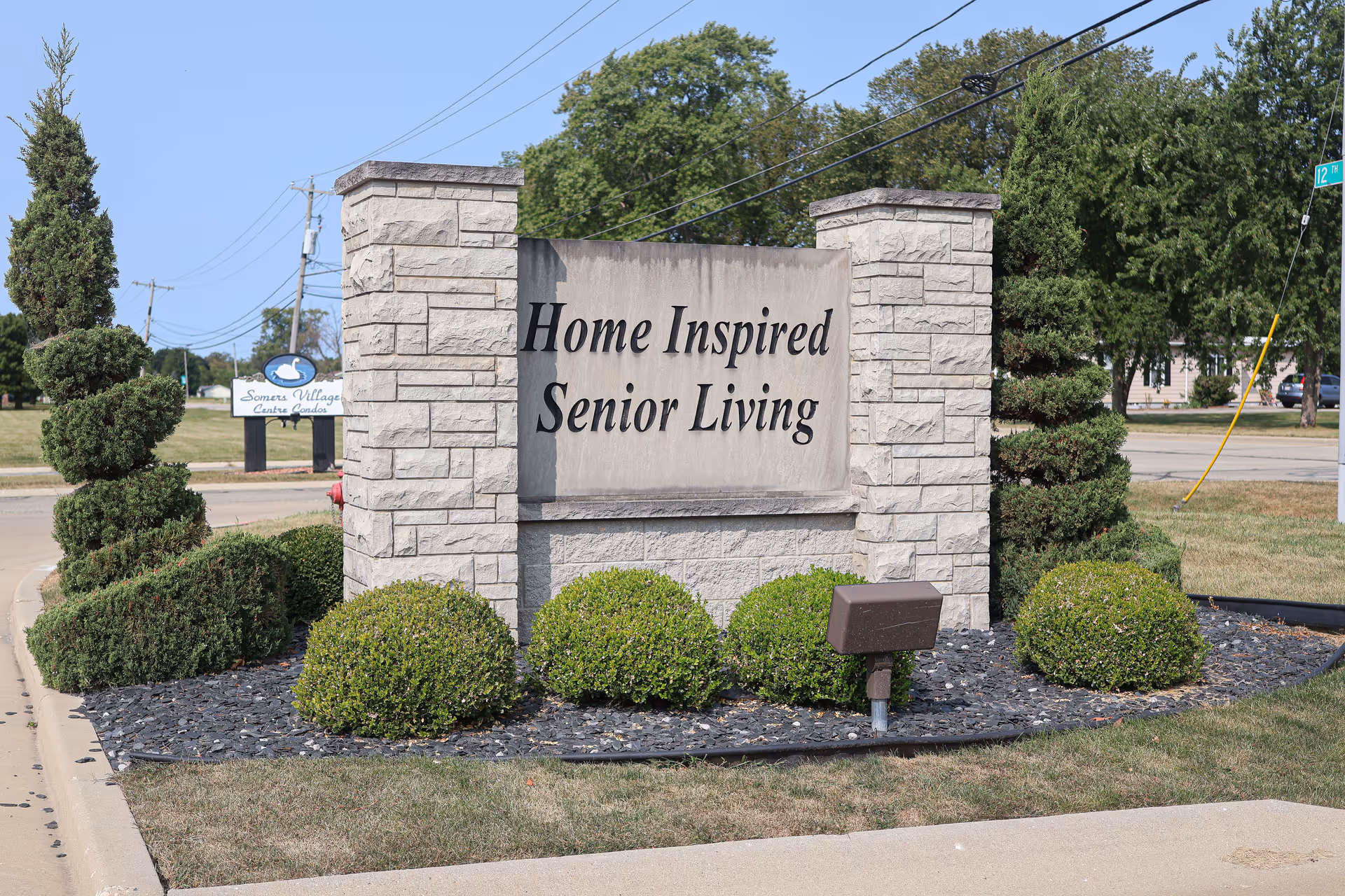 Stone monument sign reading 'Home Inspired Senior Living' with trimmed shrubs nearby.