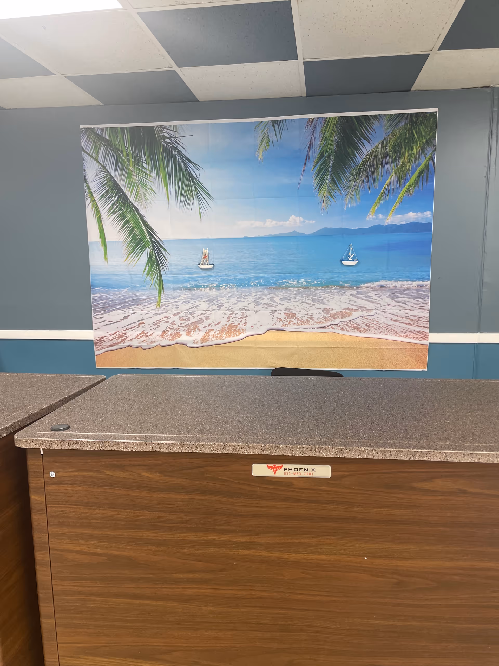 Interior lobby with a wooden counter and a tropical beach mural on the wall.