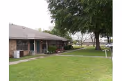 Single story brick senior living facility with green lawn and mature trees.