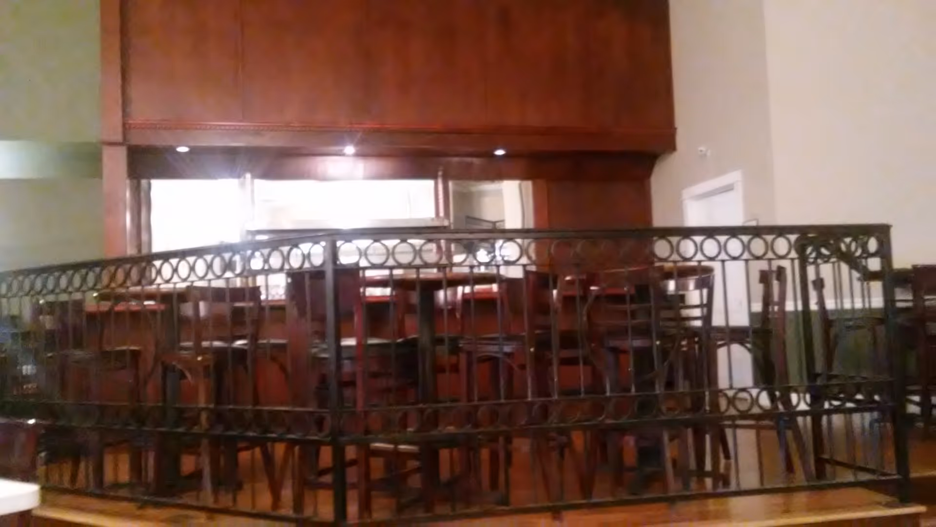 Interior dining area with wooden tables and chairs behind decorative metal railing.
