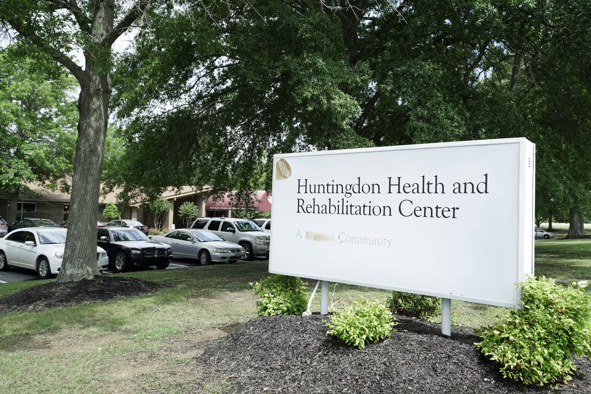 Huntingdon Health and Rehabilitation Center sign with parked cars and trees nearby.