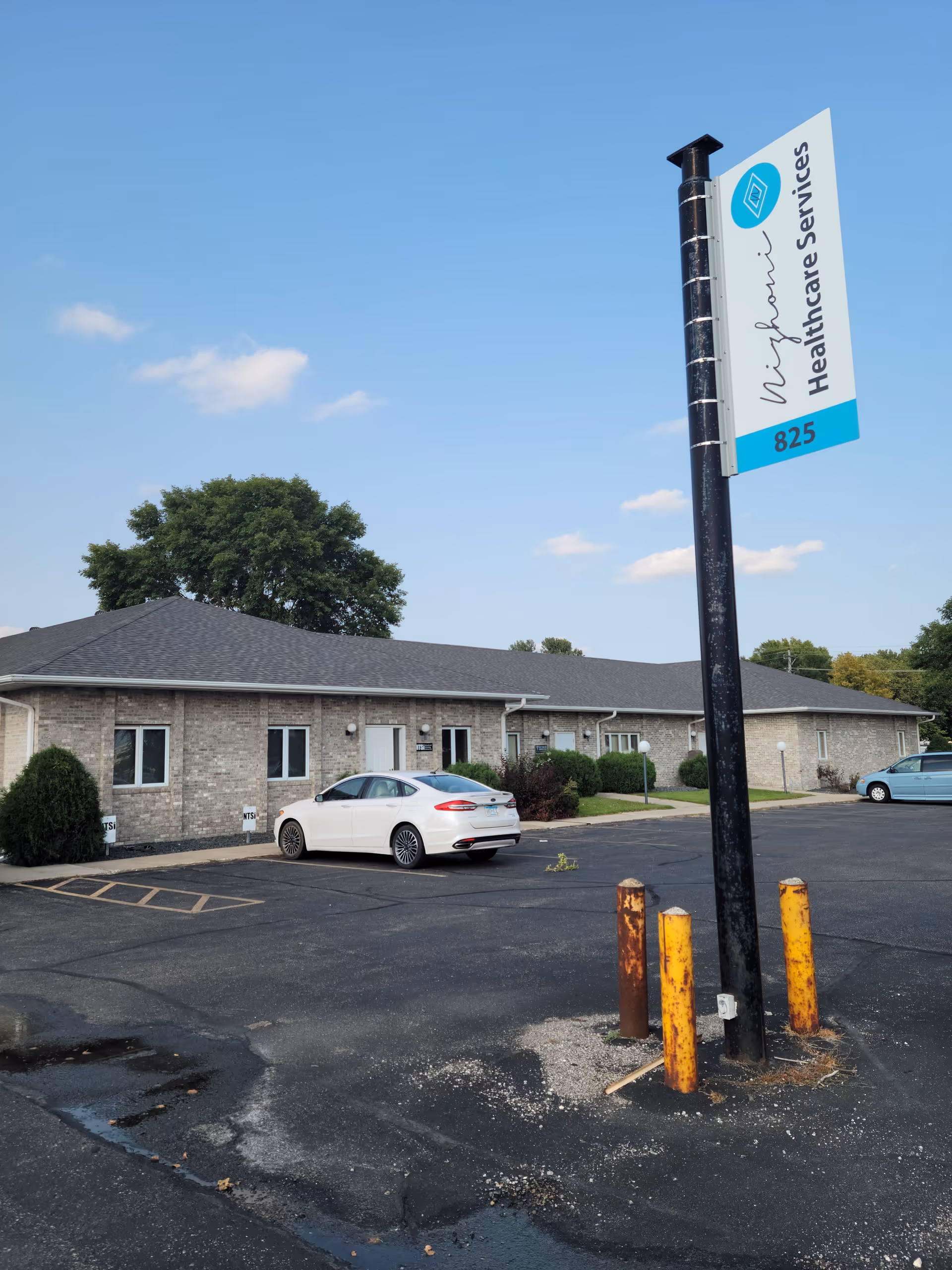 Exterior view of a single-story brick building with a parking lot and tall sign.