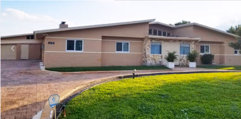 Single-story beige senior living facility exterior with curved driveway and green lawn.