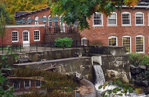 Red brick senior living exterior with arched windows, a railing terrace, and a cascading water feature.
