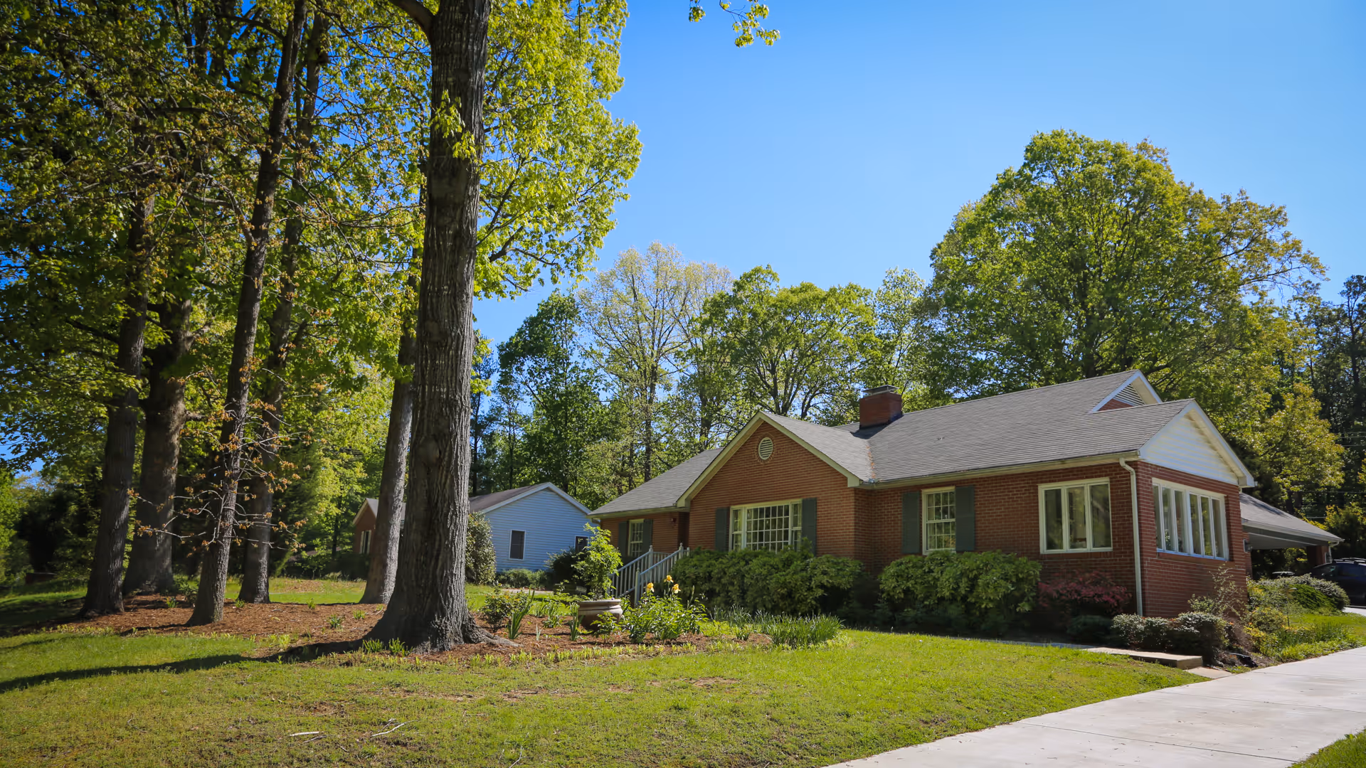 Brick Grundy Care Center building with green shutters, trees, and a driveway on a sunny day.