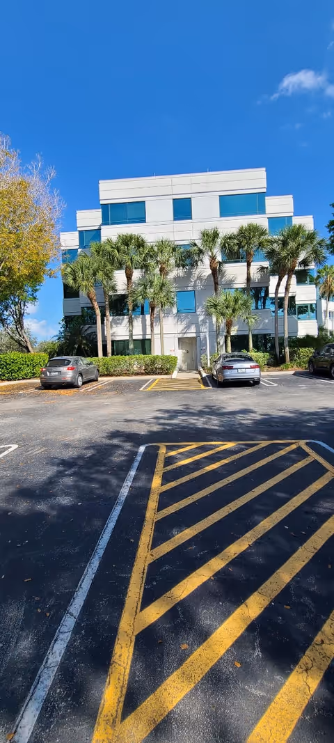 Exterior of Elite Care At Home facility: white building with palm trees and a parking lot.