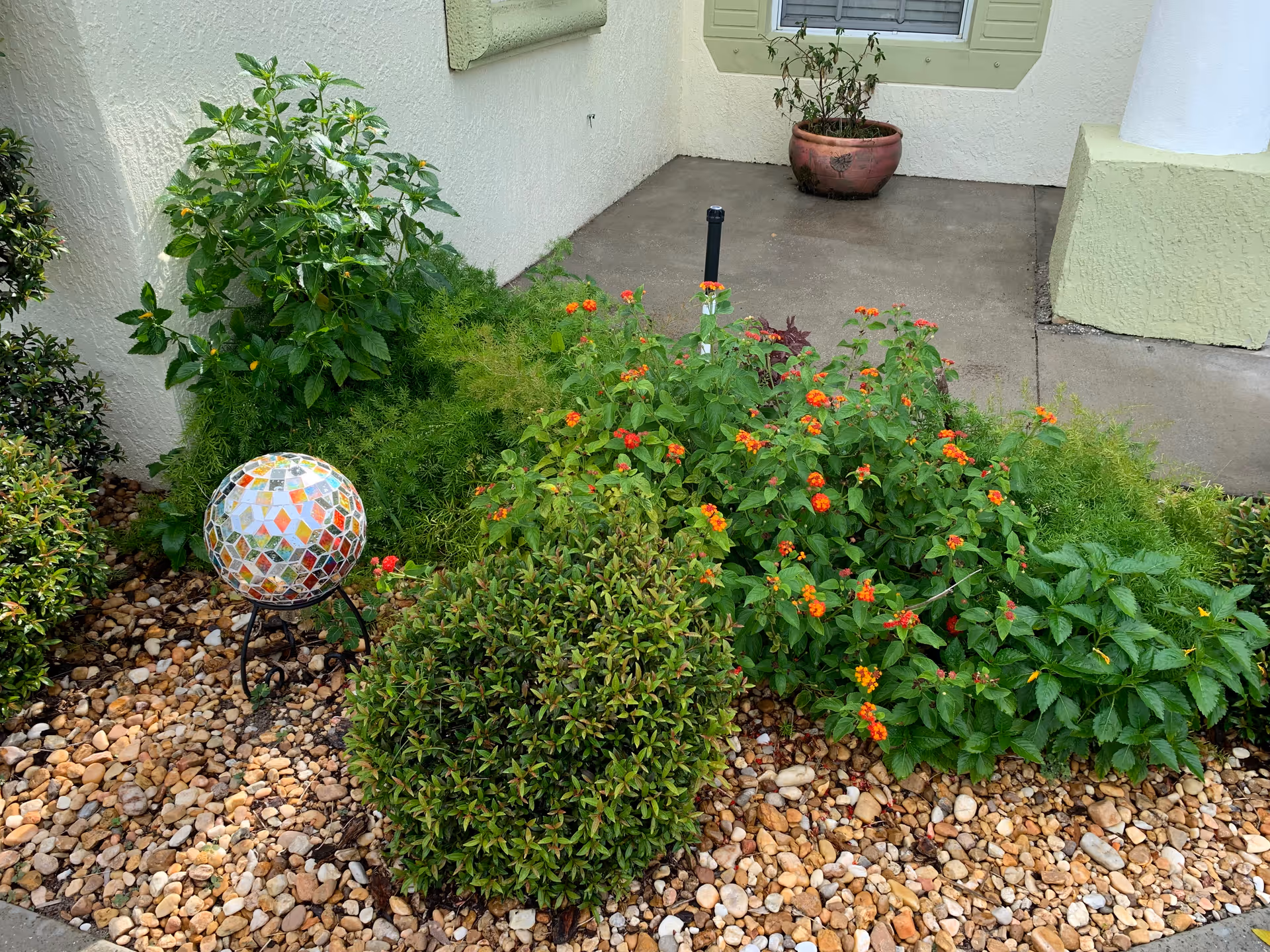 Exterior view of Sweet Home at Last entrance with plants, rocks, and a mosaic garden globe.