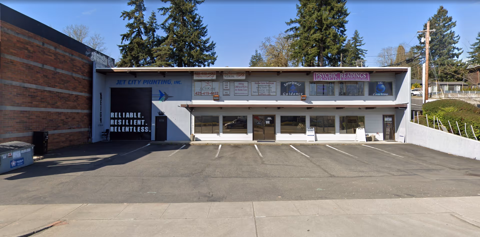 Front view of a small commercial building with glass doors, parking lot, and signs.