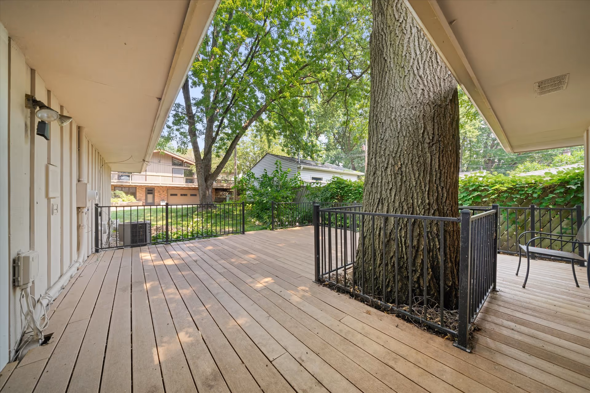 Wooden outdoor deck around a large tree, with railing and seating under a sheltered overhang.
