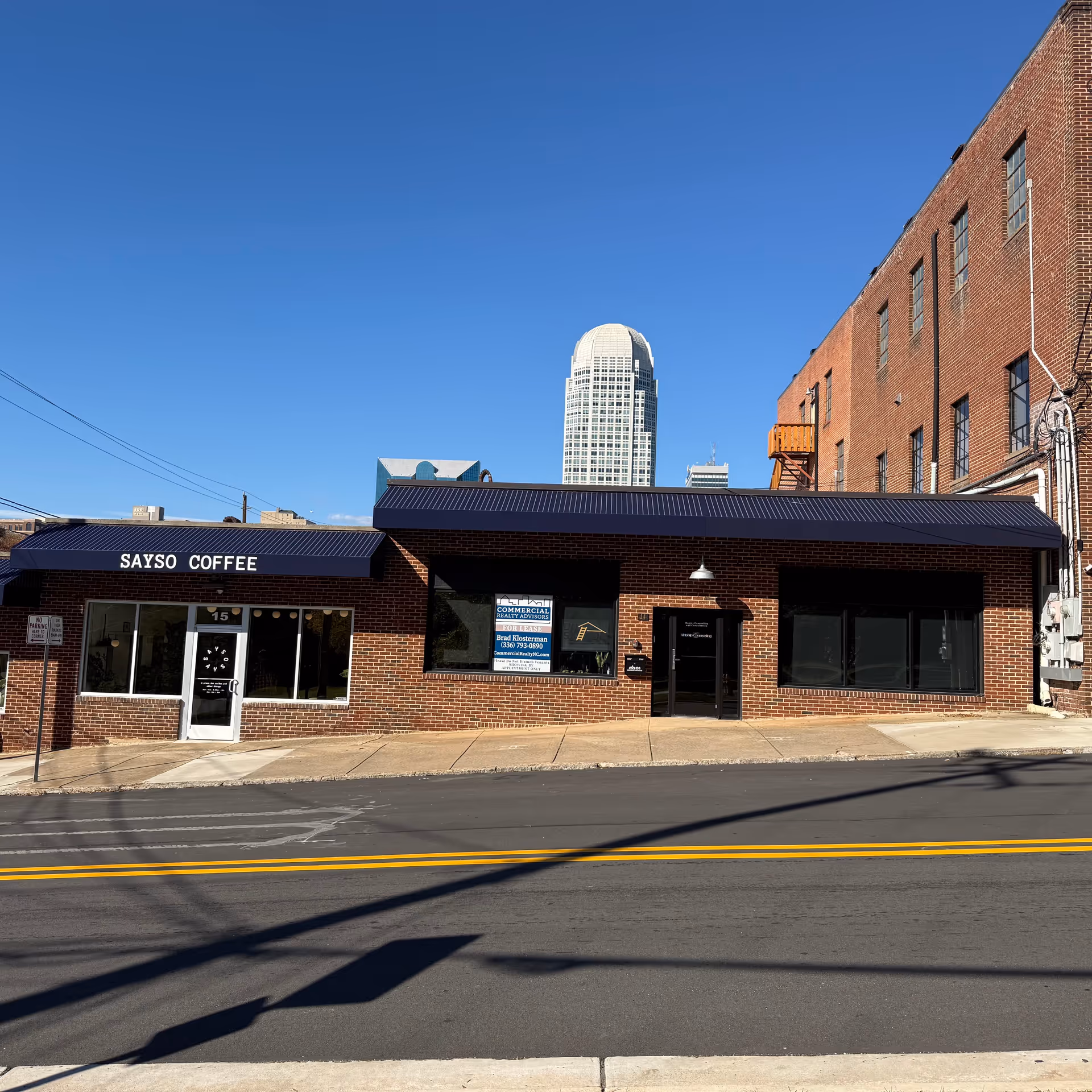 Brick storefront along a city street with a coffee shop and blue sky.