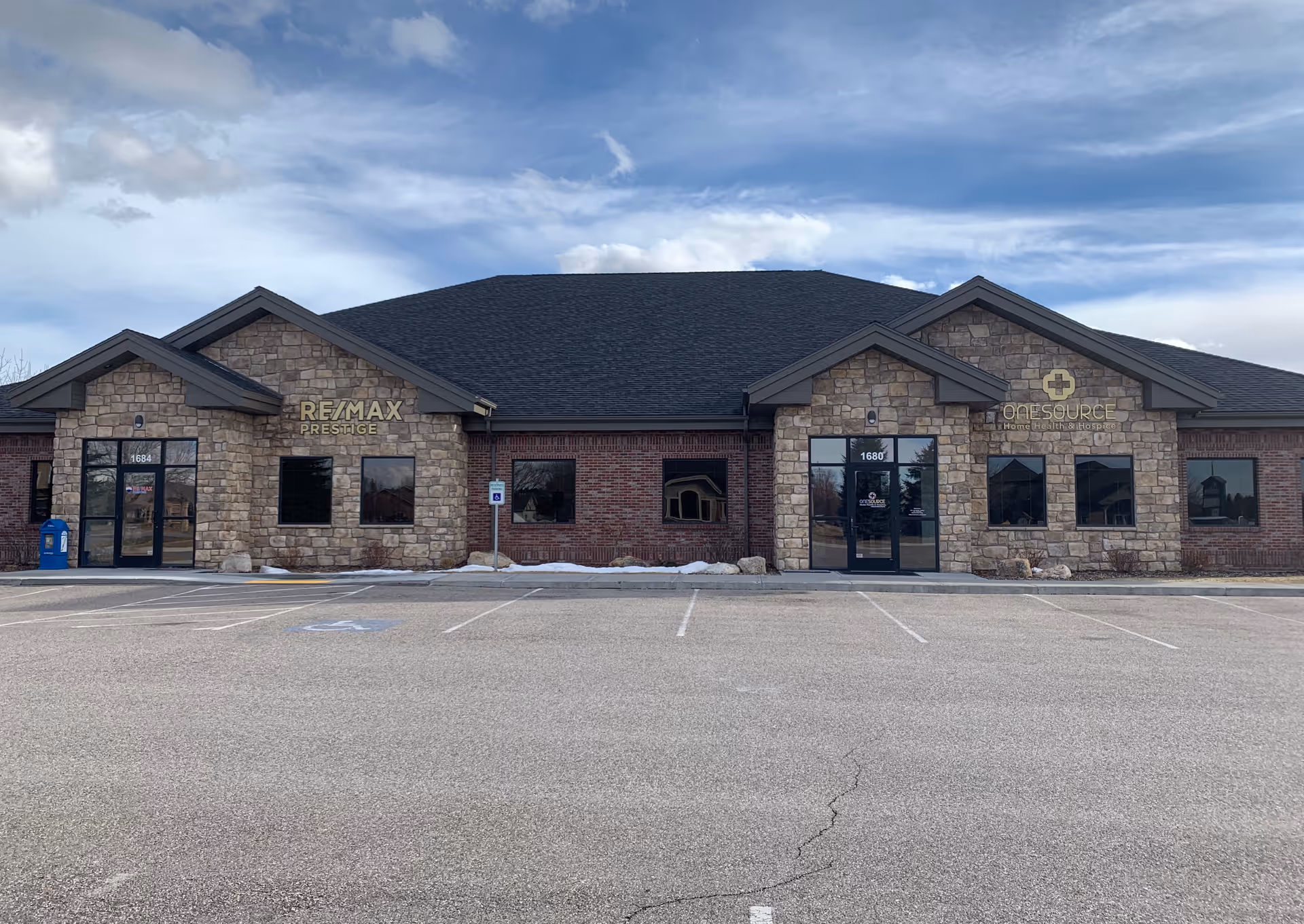 Front view of a single-story brick and stone building with OneSource sign and parking.