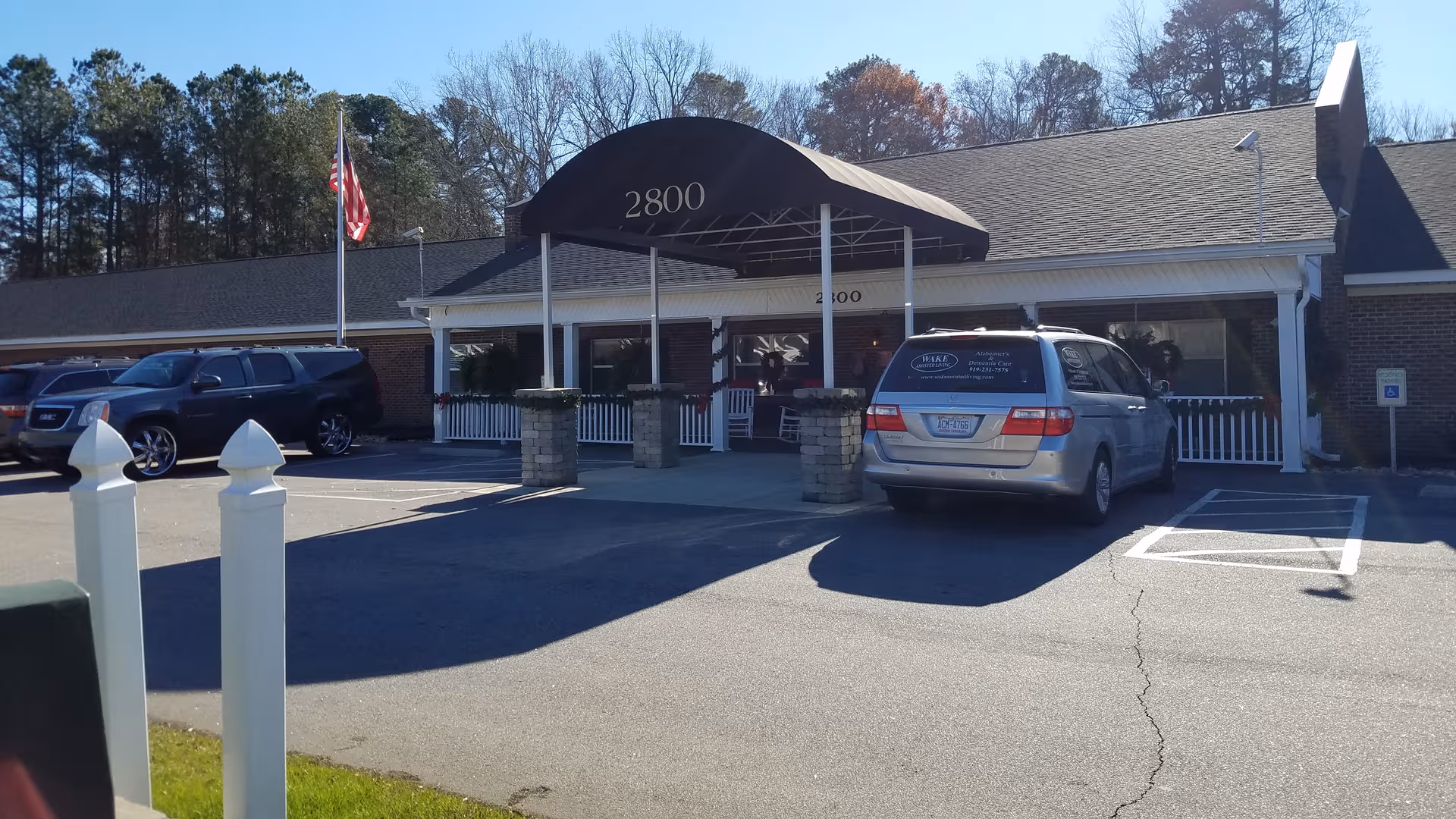 Senior living facility entrance with a covered drop-off area and parked cars