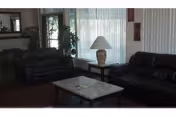 Dark leather couches surround a glass coffee table in a living room with lamp and plants