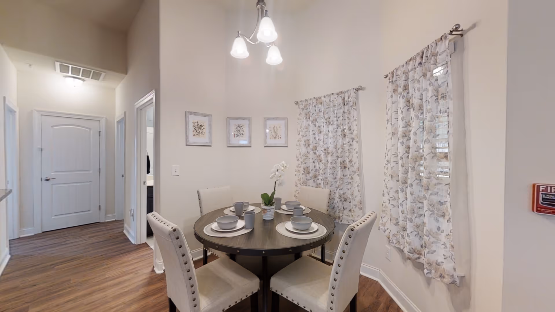 Round dining table with four place settings and floral curtains in a bright dining room.