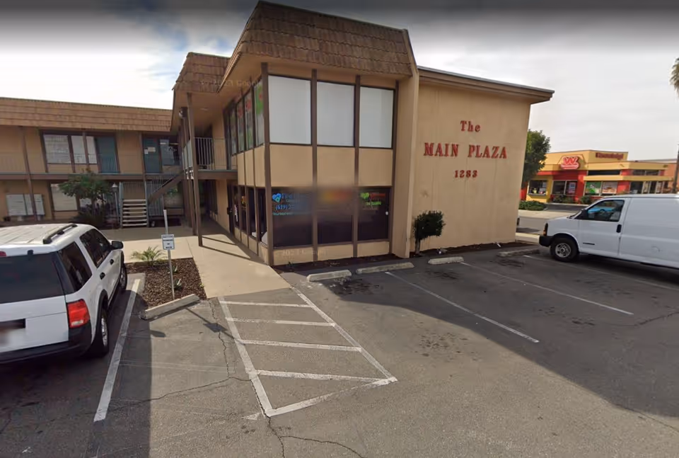 Exterior view of two-story plaza with parked cars and a beige wall reading The Main Plaza.