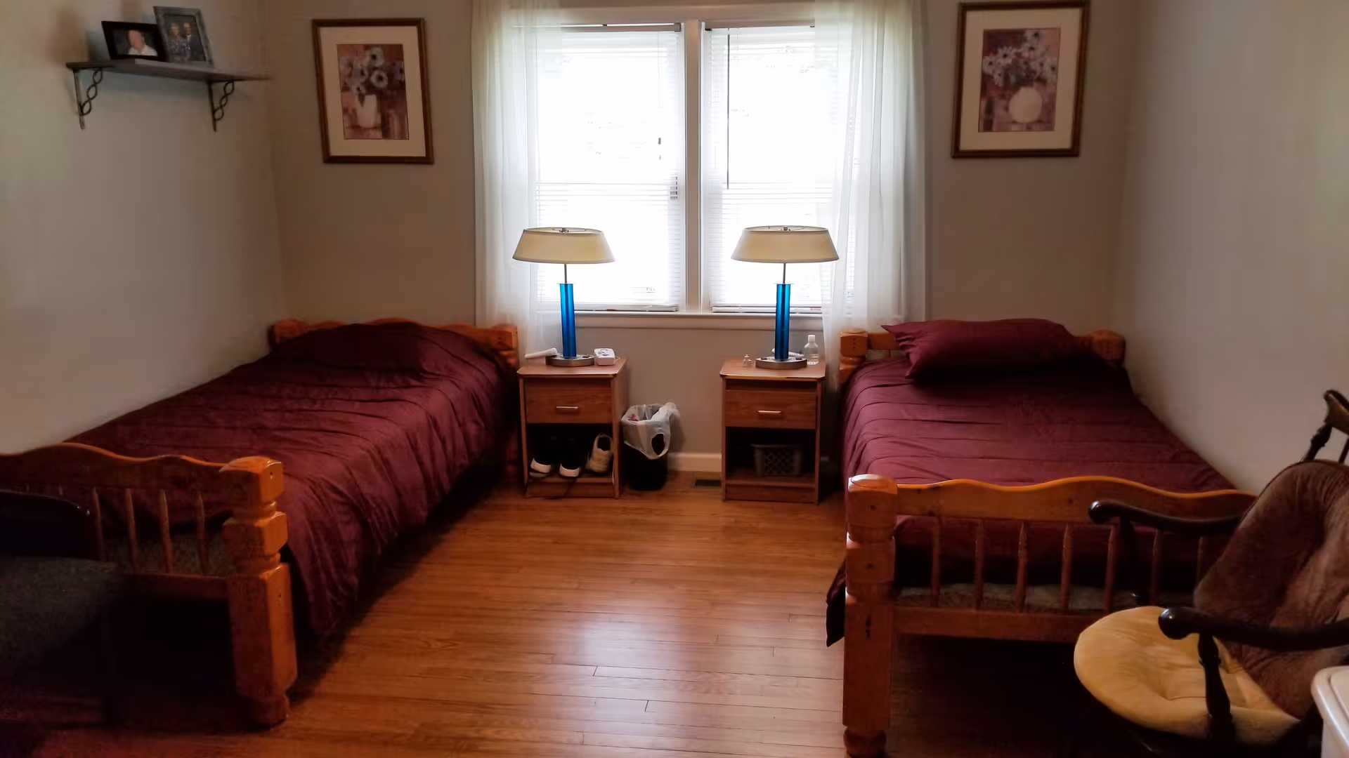 A simple shared bedroom with two twin beds, nightstands and lamps centered beneath a window.