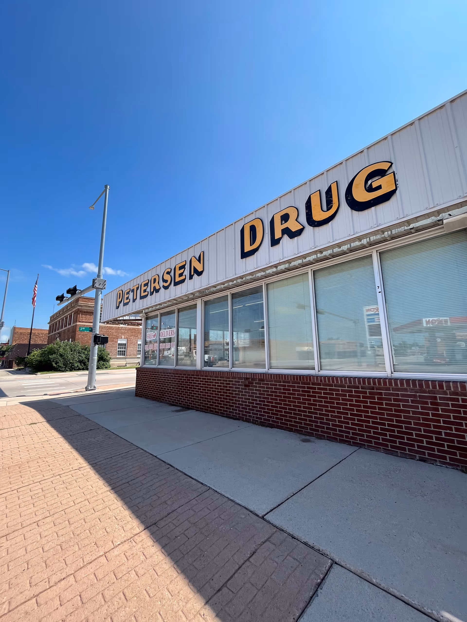 Front view of Petersen Drug storefront with brick base and large windows under clear blue sky