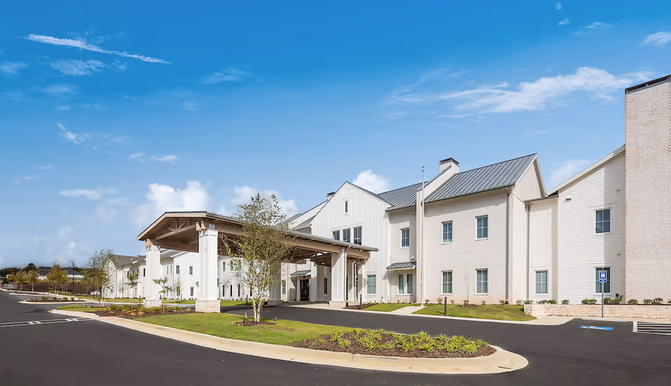White brick senior living facility with a covered entrance and adjacent parking lot.