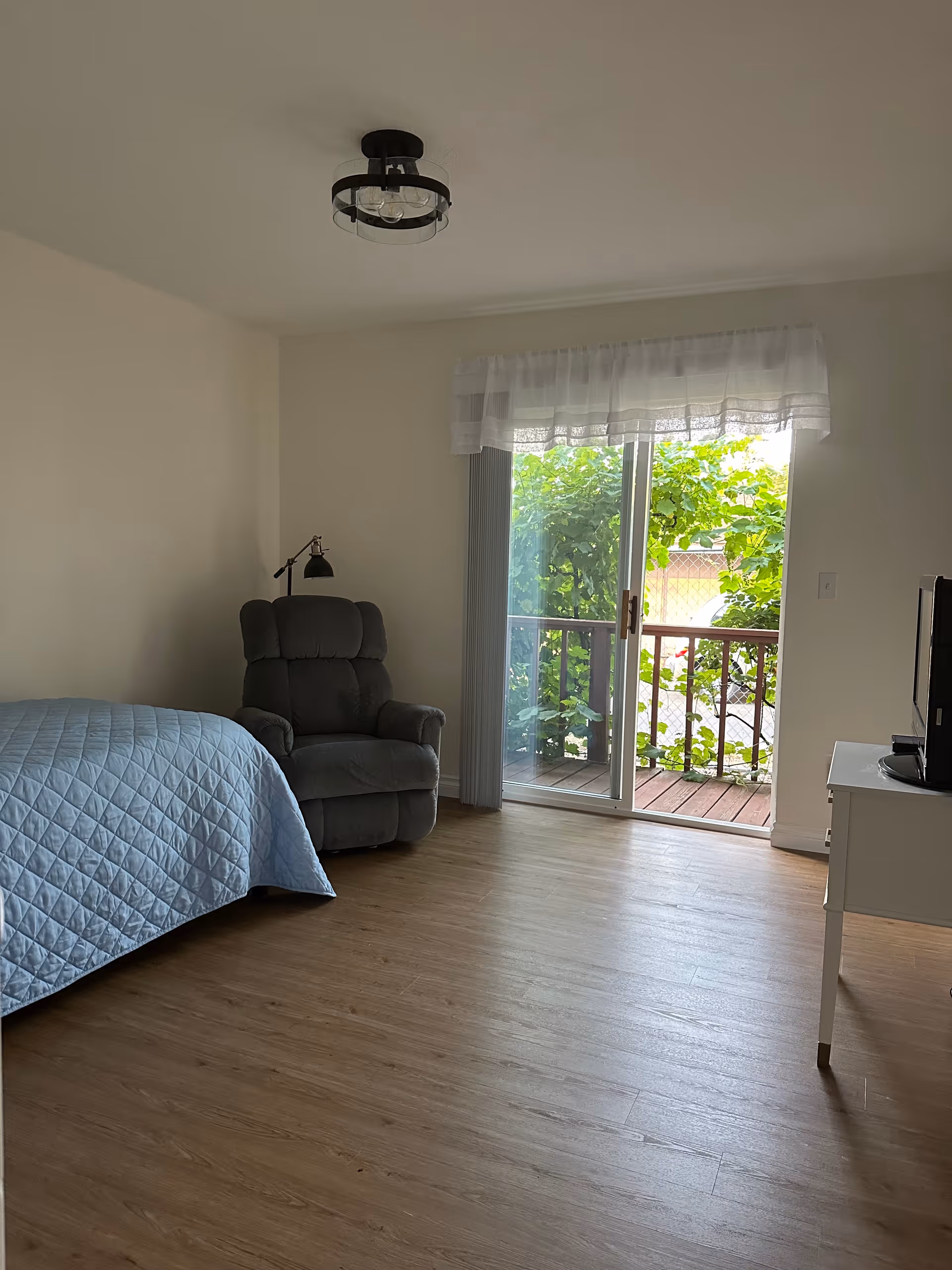 Bright bedroom with a bed, recliner, sliding glass door to a balcony, and a small desk.