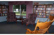 Cozy senior living lounge with bookshelves, purple chairs, and a wooden rocking chair.