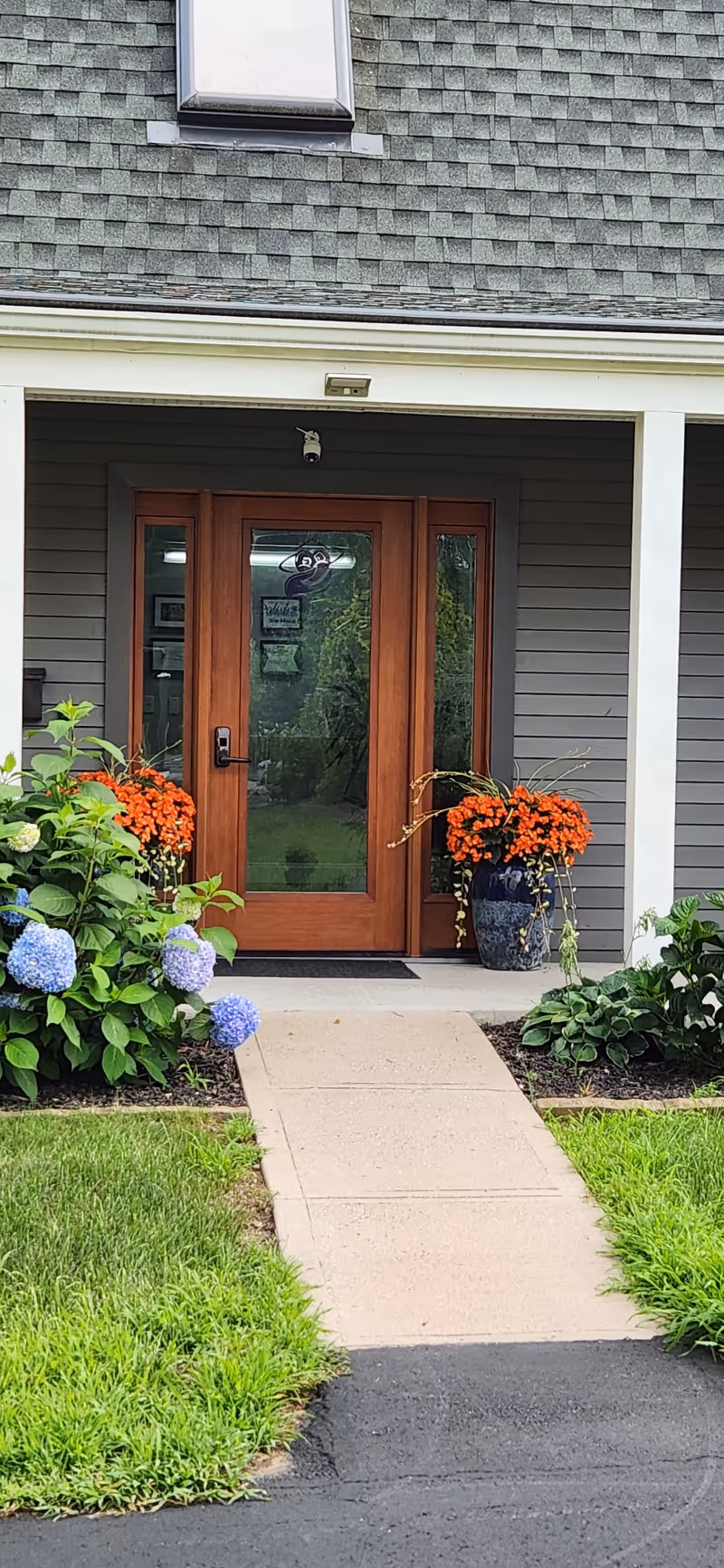 Wooden double doors frame a house-like entrance under a covered porch with potted flowers.