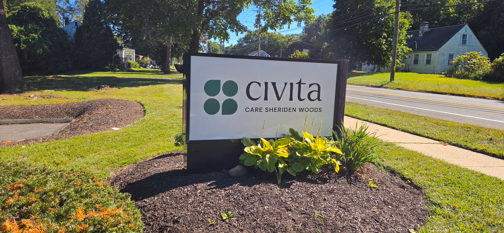 Outdoor Civita Care Sheriden Woods sign with landscaped bed and road nearby.