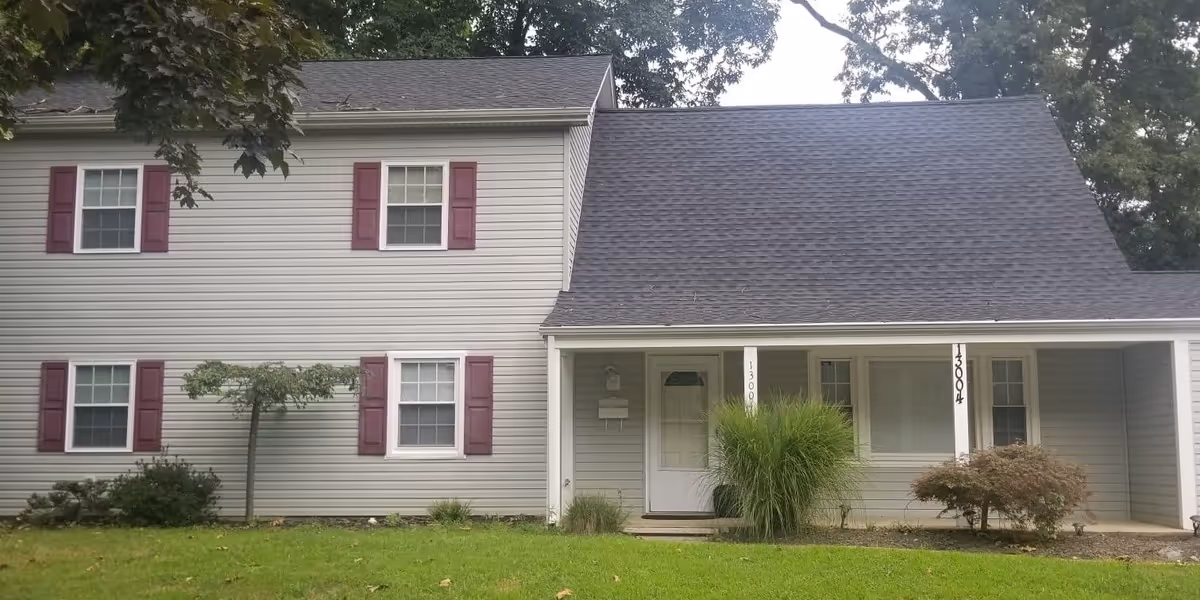 Front exterior of a two-story gray vinyl-sided house with burgundy shutters, a covered porch, and a small lawn.