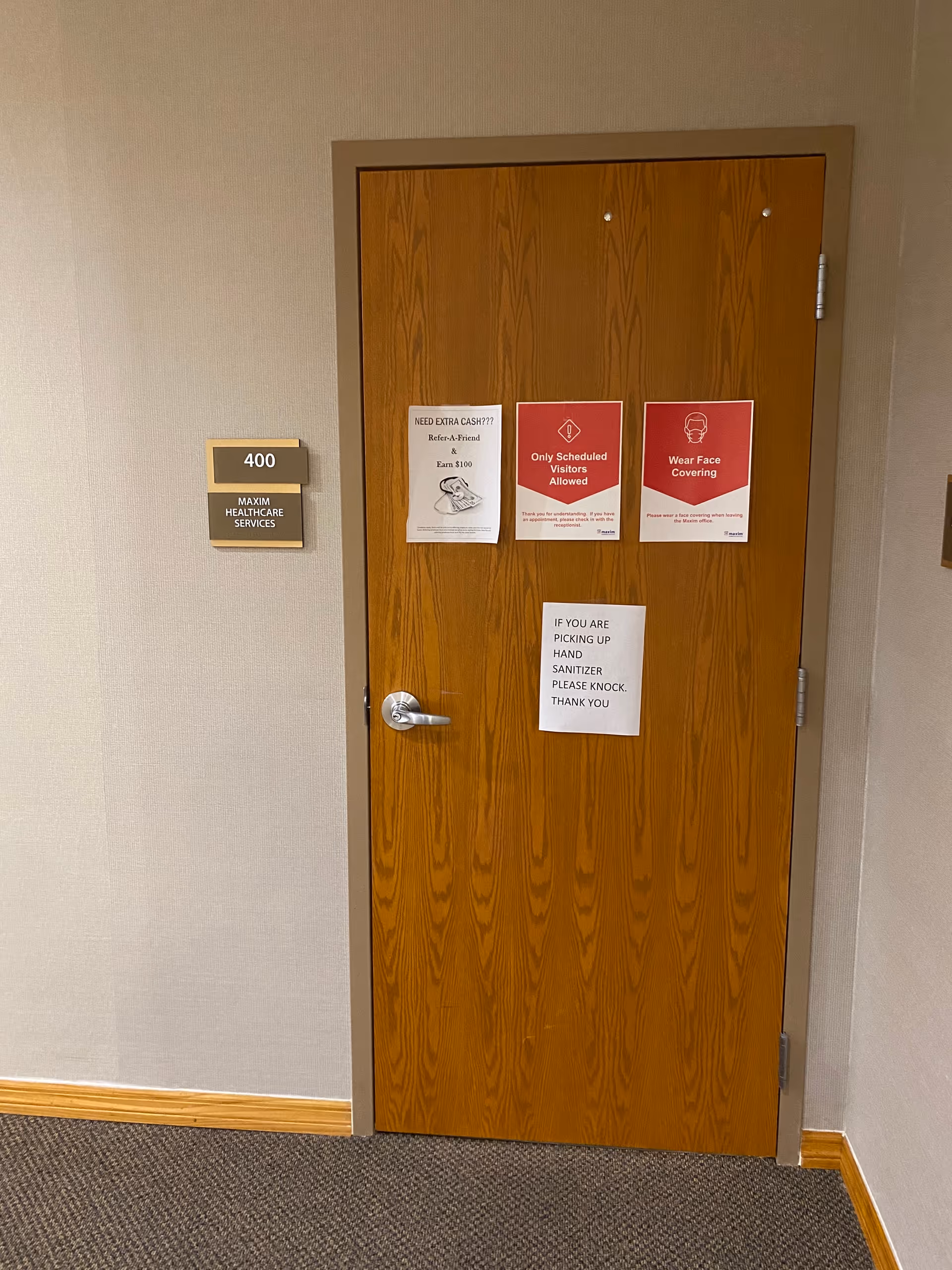 Wooden interior door with 400 label and Maxim Healthcare signage in a hallway.