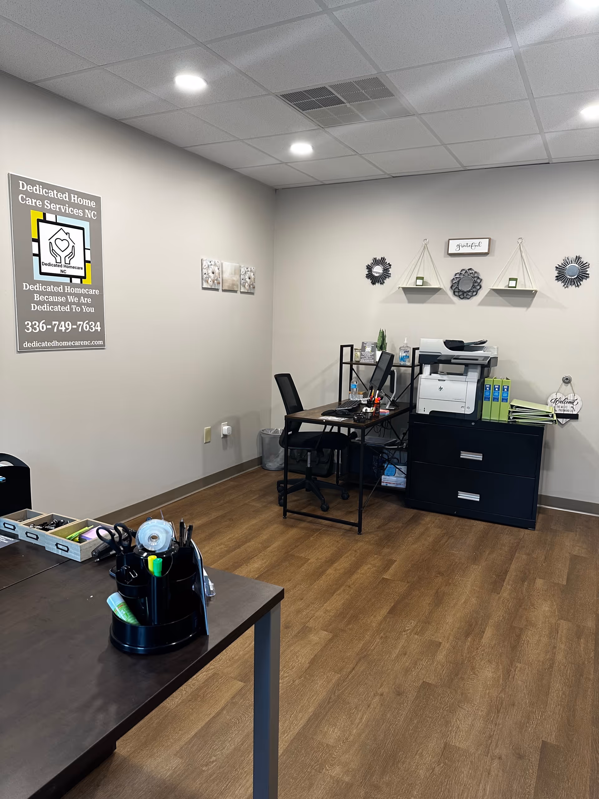 Interior office area with desks, printer, filing cabinet, and wall decor in Dedicated Homecare NC.