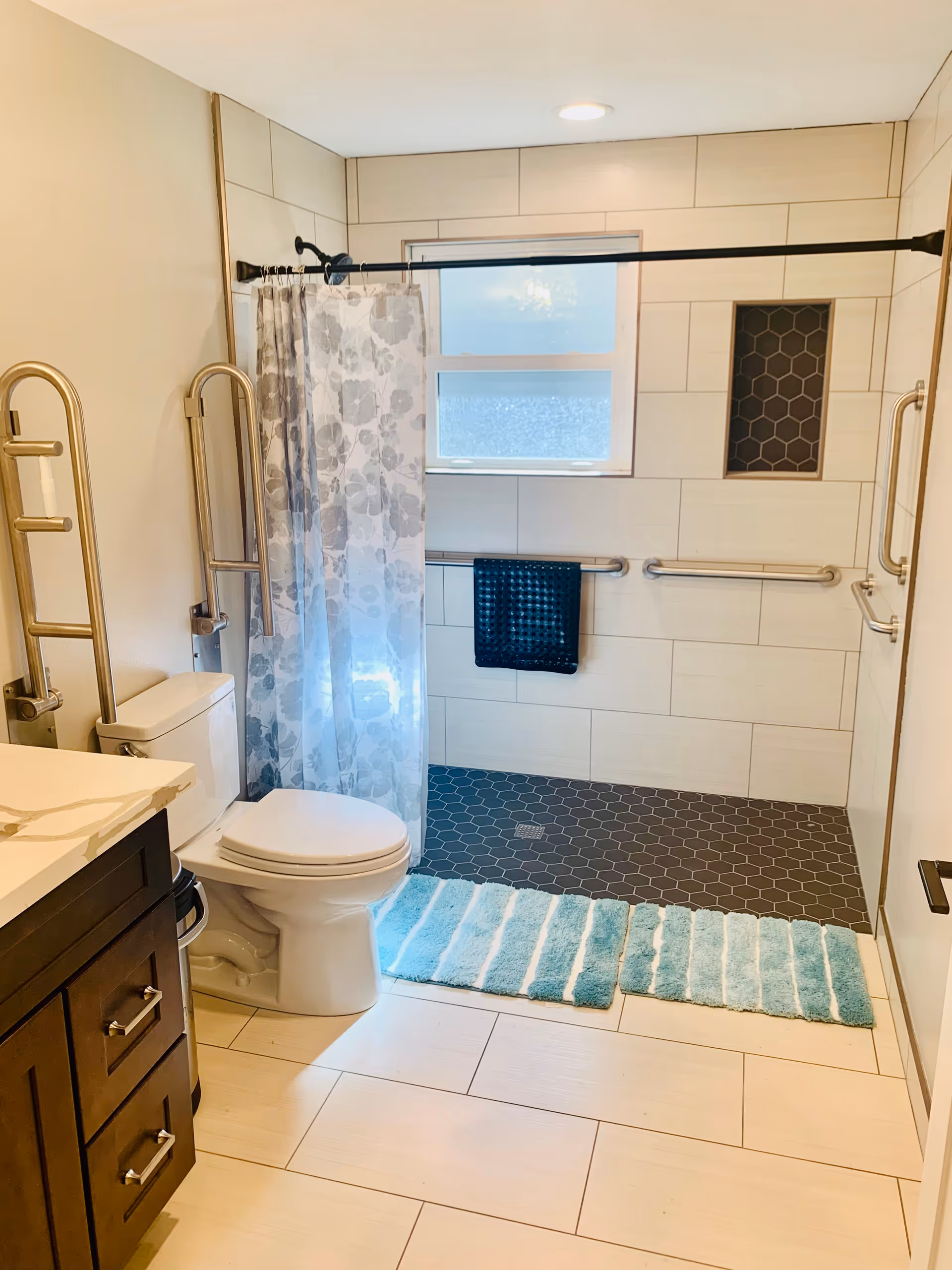 Bright accessible bathroom featuring a shower with curtain, toilet, grab bars, and blue bath mats.