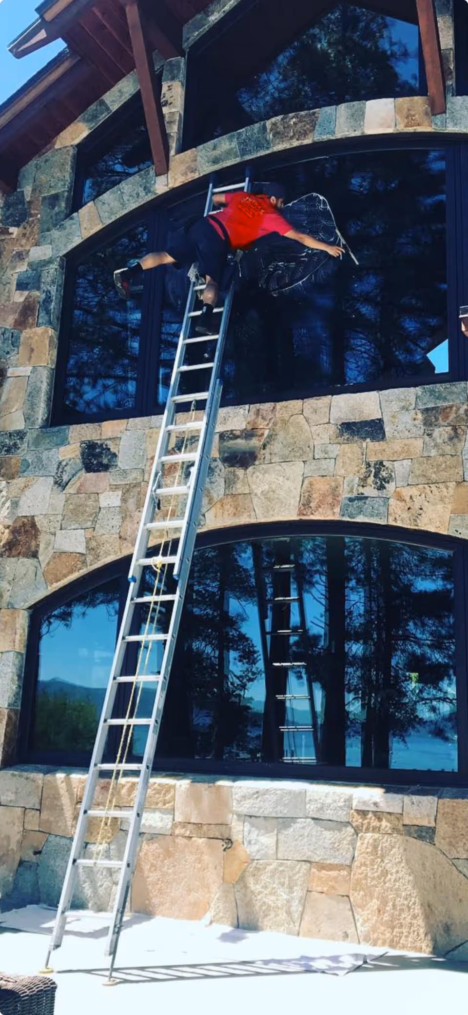 Worker on a ladder cleans a large arched window on a stone building exterior.