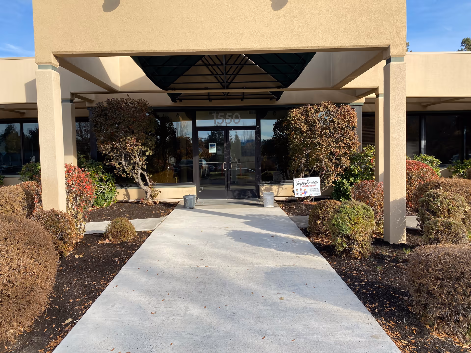 Entrance to a facility with a covered walkway and manicured shrubs.