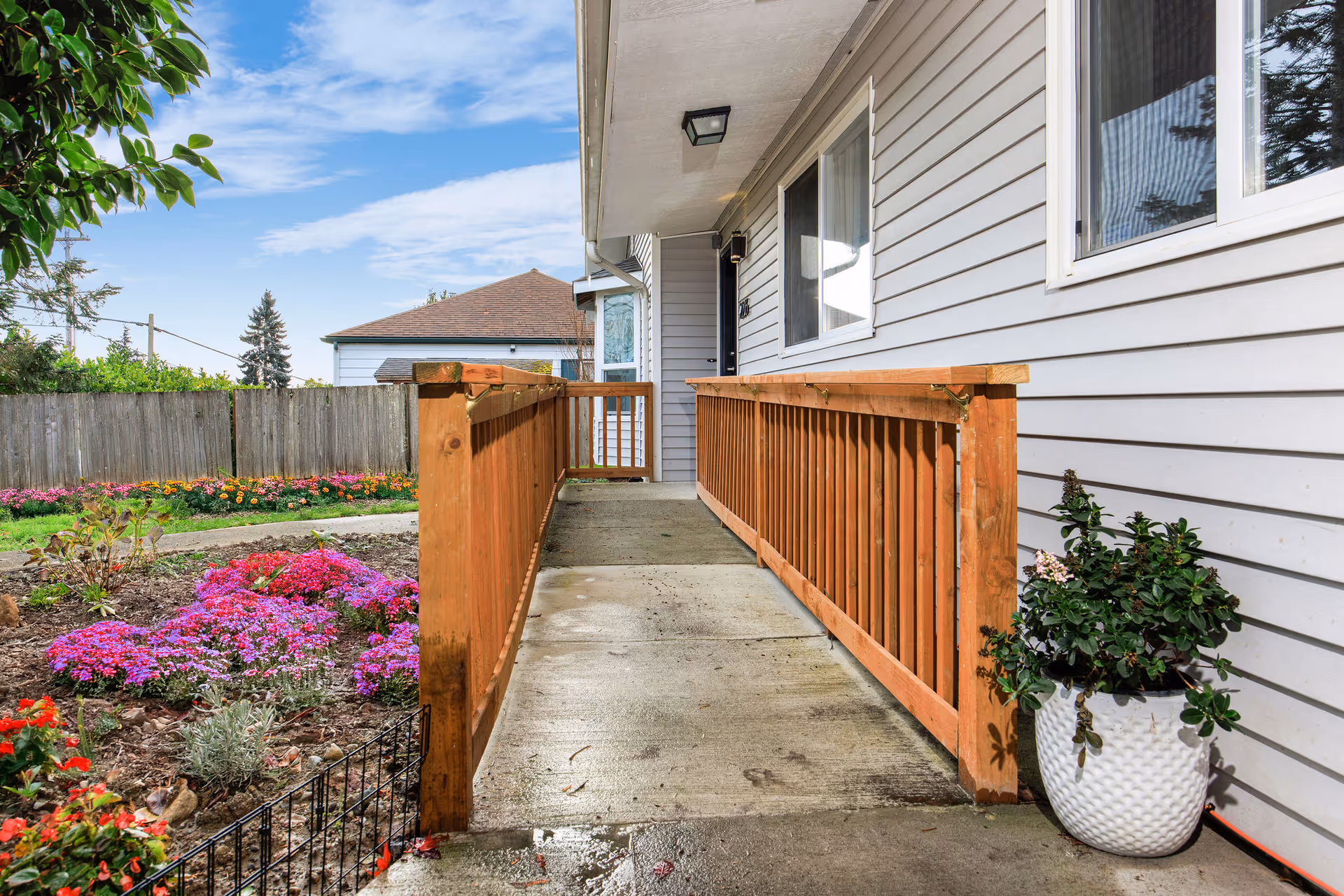 Front entrance of a senior living home with a wooden ramp and blooming garden.
