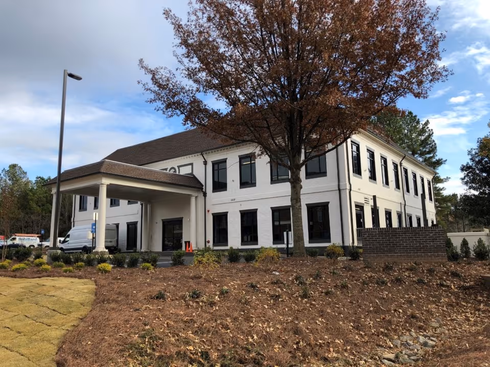 White two-story building with black-framed windows, a covered entrance, and landscaped surroundings.