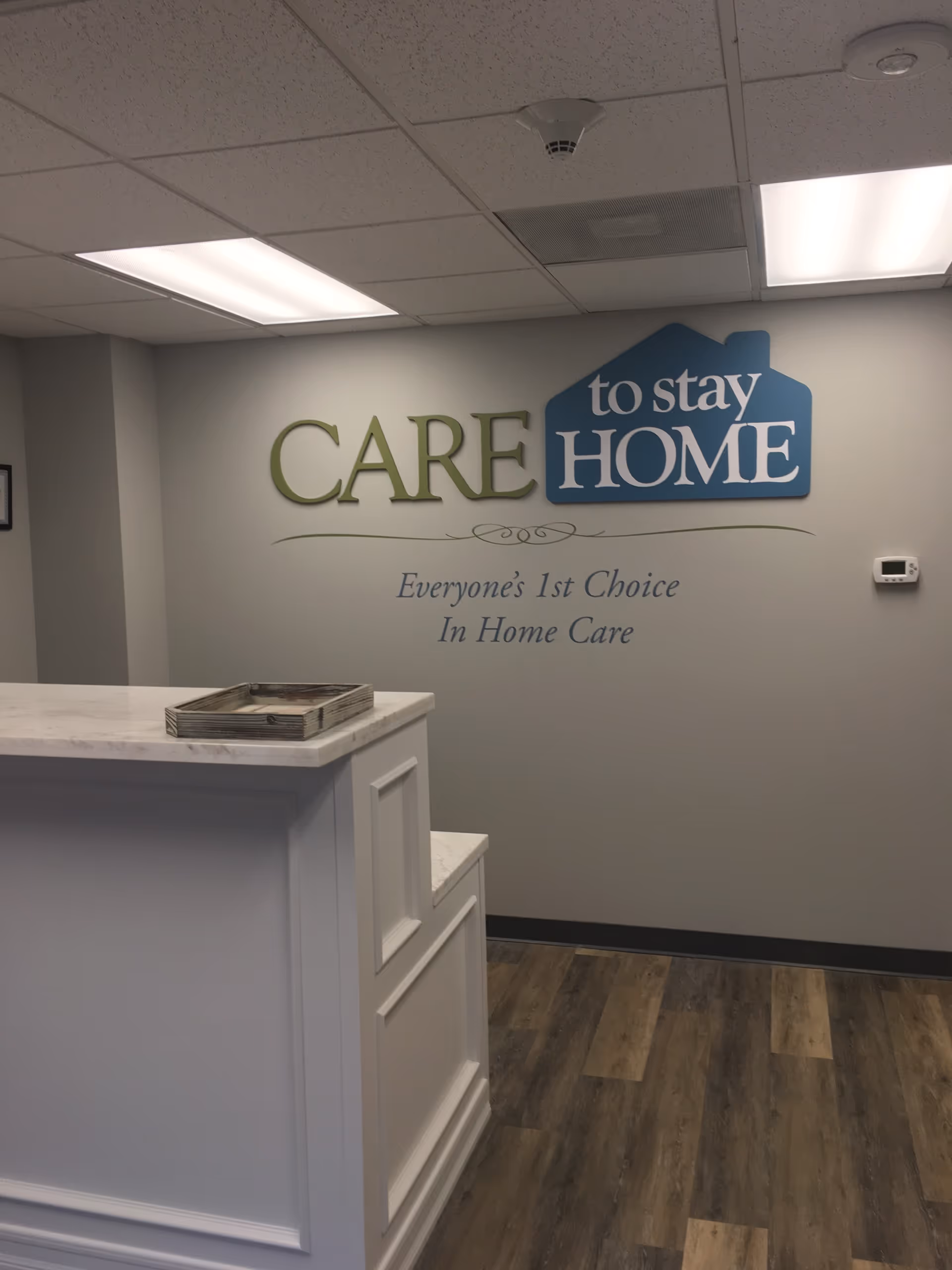 Reception desk in a care home lobby with a wall logo reading Care To Stay Home