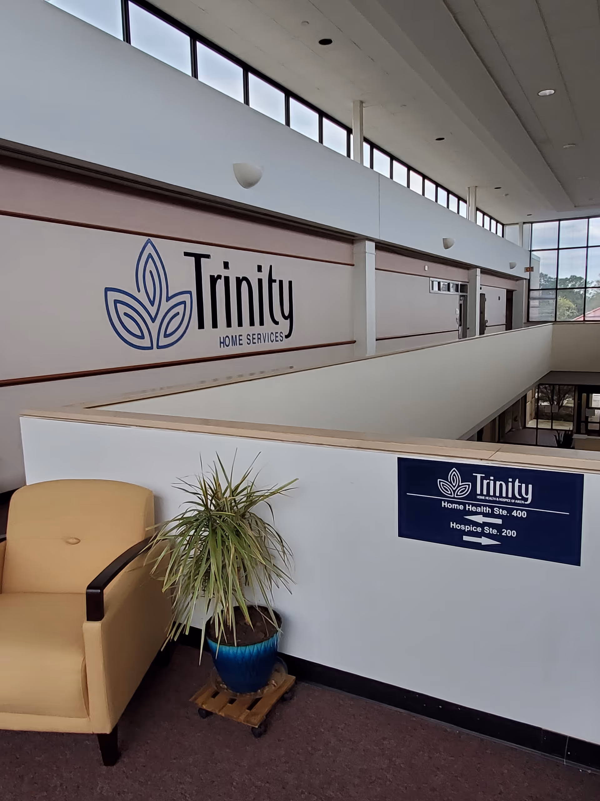Interior hallway displaying Trinity Home Health branding, seating, and a potted plant.