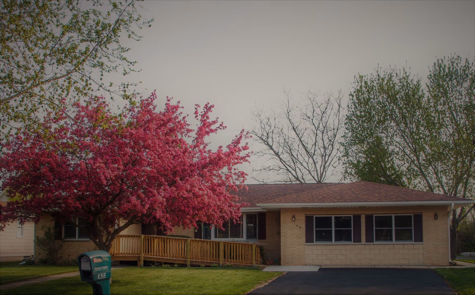 Front view of a single-story brick senior living facility with a pink flowering tree and ramp.