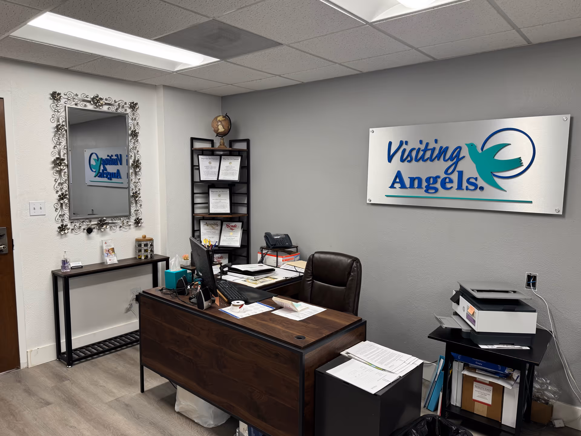Office interior at Visiting Angels with desk, computer, sign, and certificate shelf.