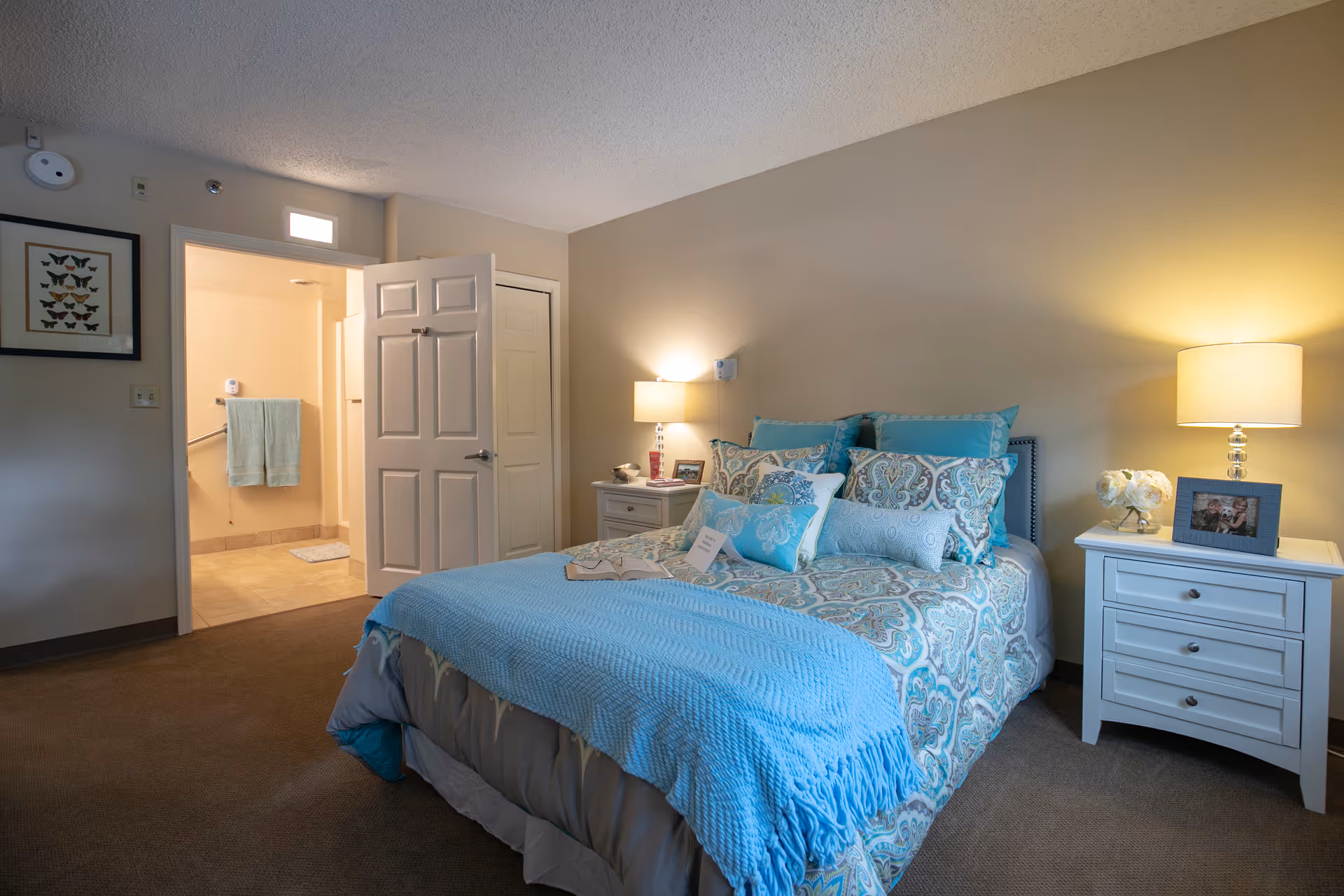 A neatly made bedroom with blue patterned bedding and two white nightstands.
