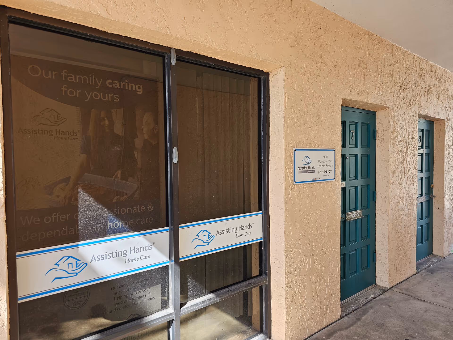 Beige building exterior with two teal doors and storefront window displaying Assisting Hands signage.